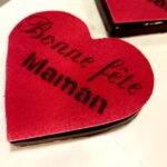 Red heart-shaped craft/valentine cutout with black writing rests on a white surface, suggesting a handmade card or decoration.