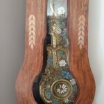 Ornate antique grandfather clock case with carved wood and colorful floral inlay visible through the glass panel